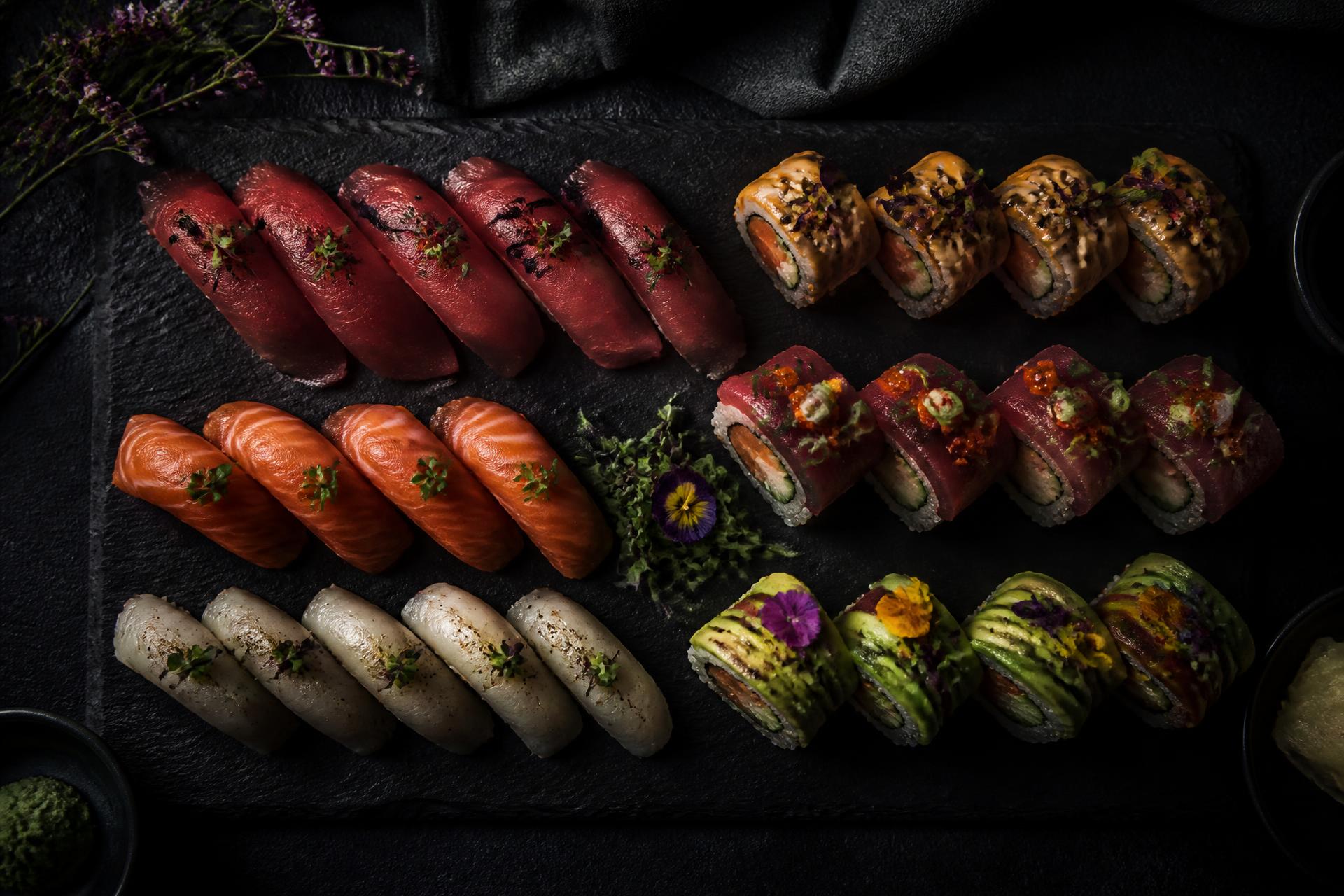 An assortment of nigiri and specialty sushi rolls plated on dark slate at Nobu Sushi.